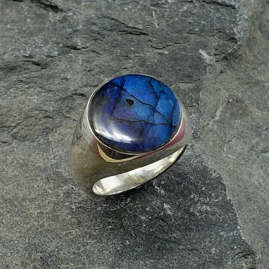 A heavy silver signet ring set with an oval labradorite cabochon flashing blue, on grey slate.