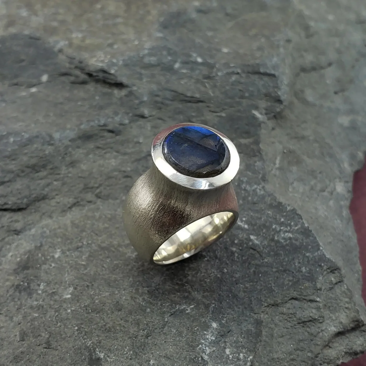A brushed silver tower ring set with an oval labradorite cabochon, photographed on slate.