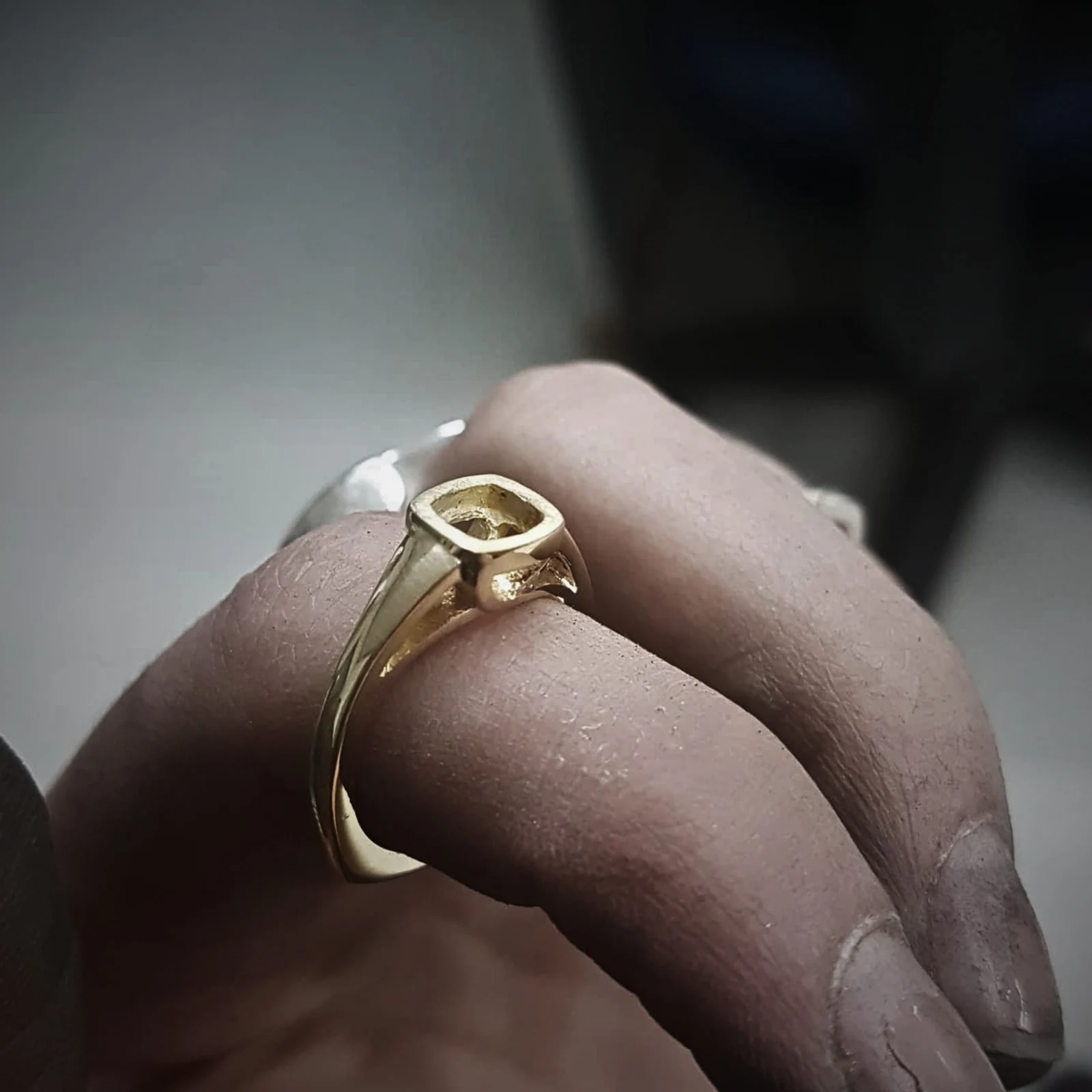 The same ring part way through fabrication, in yellow gold with the bezel still empty, tried on a hand at the bench.